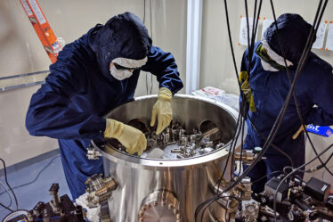 Two people in clean suits inspecting a mirror-testing apparatus.