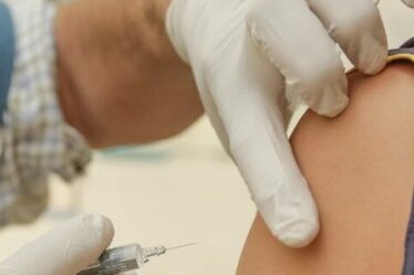 Healthcare worker steadies needle in preparation for injecting vaccine into patient's shoulder.