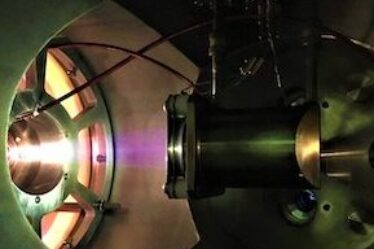 A picture of the ion source used by the IsoDAR cyclotron team, which shows the ion beam glowing inside their device.