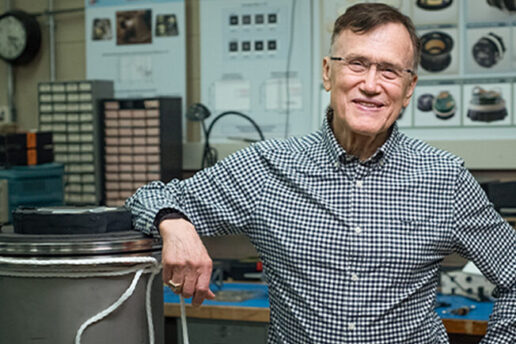 George Ricker stands in a lab, resting his elbow on a large metal cylinder