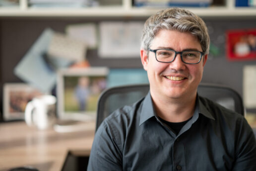 Professor Michael McDonald smiles while sitting at his desk, with blurry office background.