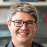 Professor Michael McDonald smiles while sitting at his desk, with blurry office background.