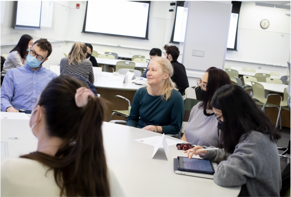 Professsor Rigos sits at table in classroom with students