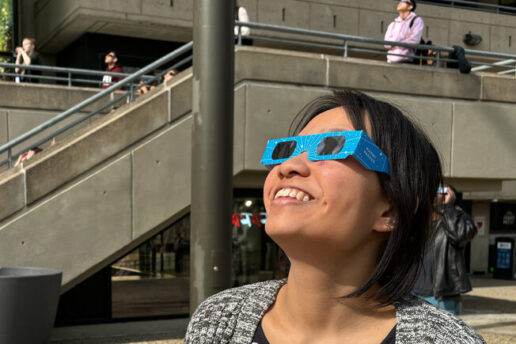 Joanna Chen wears special eclipse glasses and look up, with other people doing the same in background.