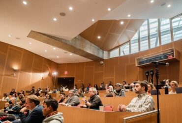 View of audience members in a lecture hall, who look to be listening intently to the panel discussions.