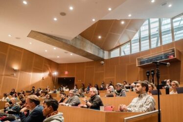 View of audience members in a lecture hall, who look to be listening intently to the panel discussions.