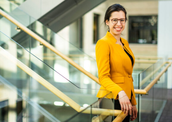 Netta Engelhardt stands near stairway for a portrait. Dramatic diagonal shapes are created by the stairways and glass railings.