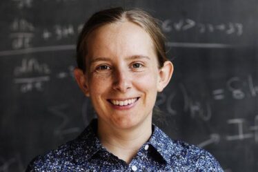 Tracy Slatyer poses in front of blackboard covered in physics equations