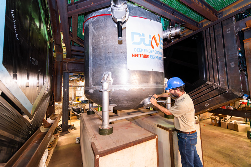 A person in a blue hard hat working on the detector.